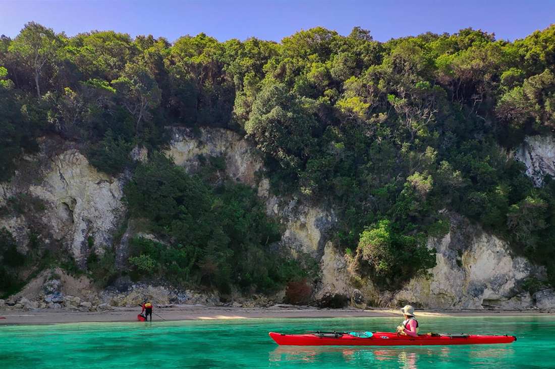 A red sea kayak on the turquoise water of the Blue Lagoon below wooded cliffs, the highlight of a Sivota sea kayak tour.