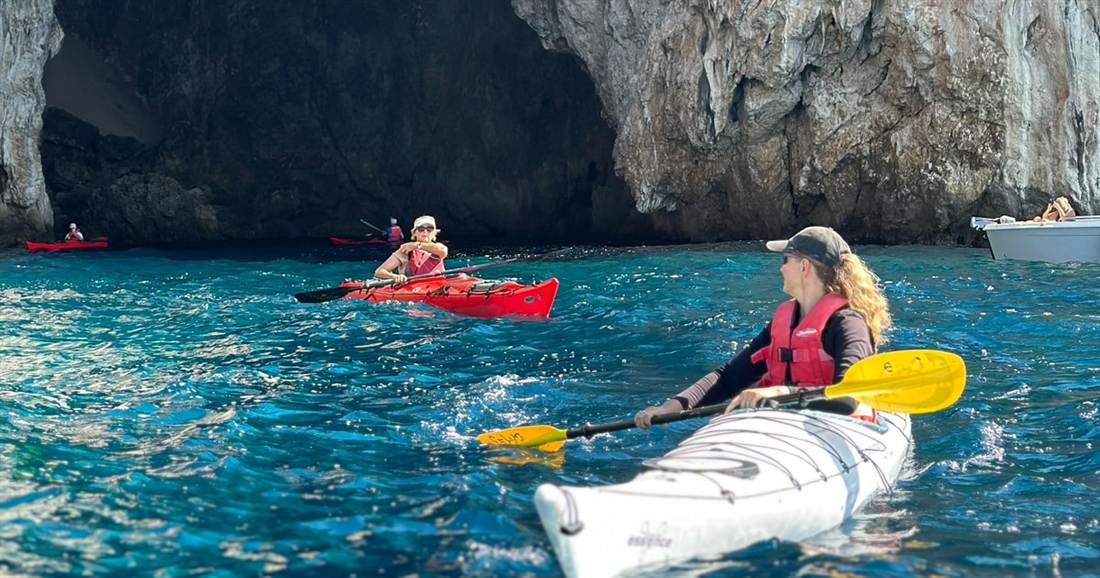 Two paddlers in sea kayaks by a sea cave on the Sivota coast, part of the Sivota sea kayak route.