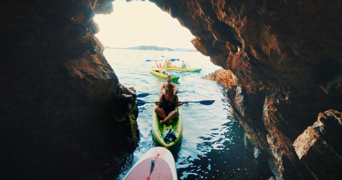 A kayaker paddling through a narrow sea cave arch towards open water on a Skiathos kayak tour.