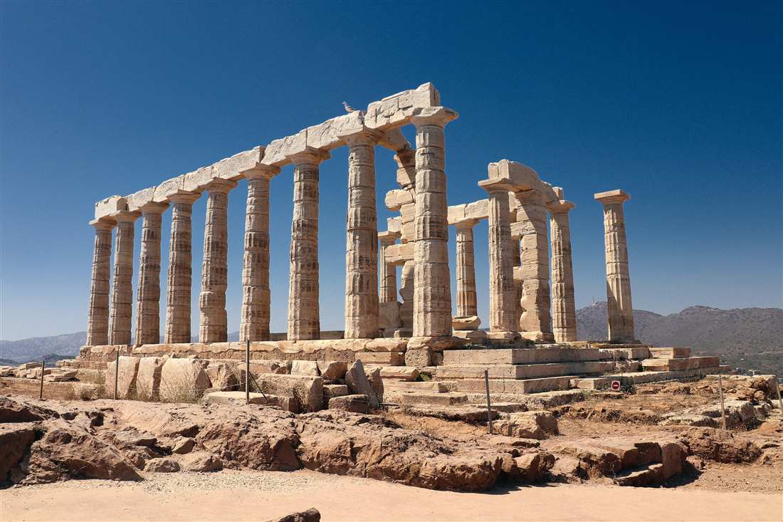 The marble columns of the Temple of Poseidon standing whole on Cape Sounion under a deep blue sky