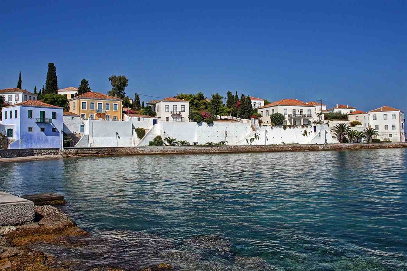 Spetses town seafront with white captains mansions above clear turquoise water