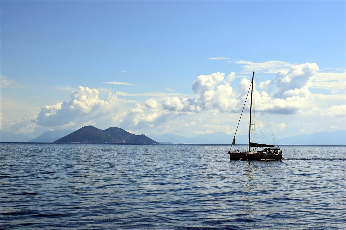 A sailing boat crossing the calm Ionian Sea toward the island of Atokos, the route of the swimming pigs Lefkada cruises from Nydri.