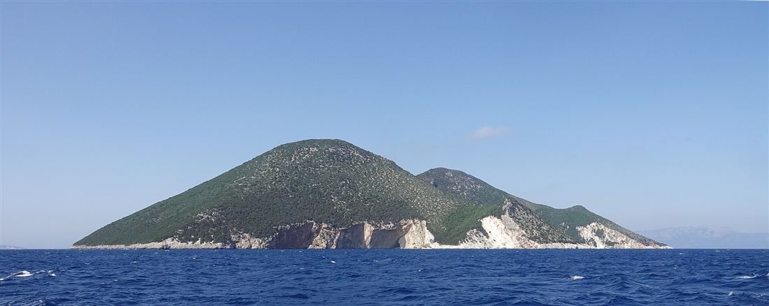 The green hills and white cliffs of Atokos rising from the Ionian Sea, the island where the swimming pigs Lefkada cruises stop.