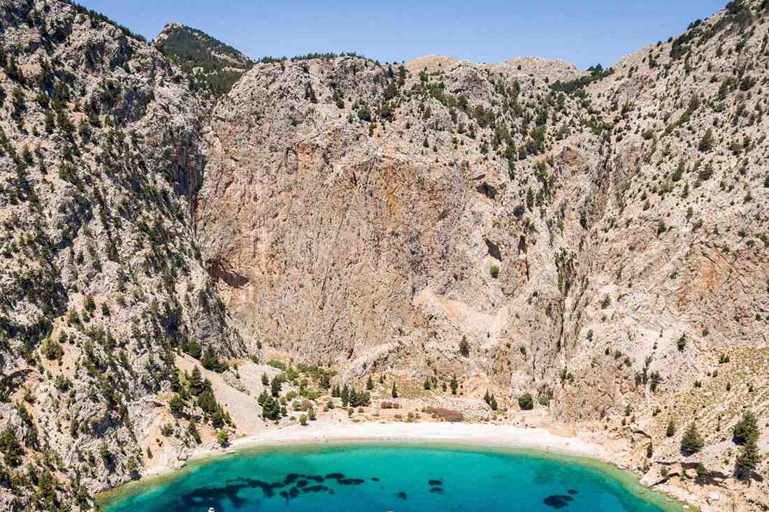 Aerial view of a turquoise cove with a pebble beach below steep rocky cliffs