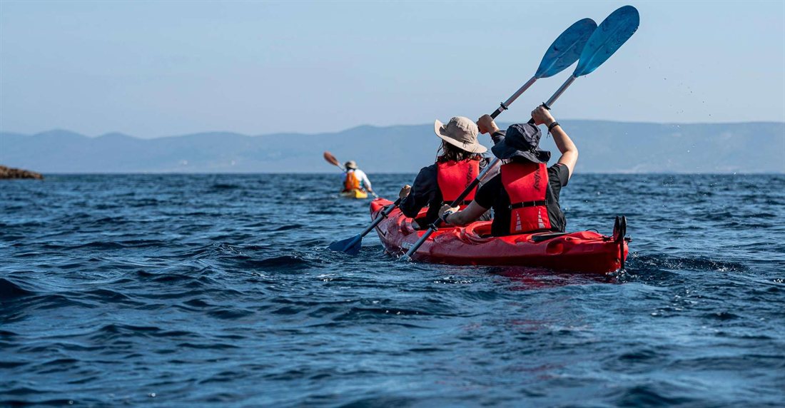 Two paddlers in red life jackets in a tandem sea kayak heading toward a distant island coastline