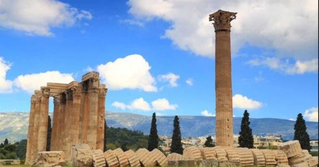 The standing Corinthian columns of the Temple of Olympian Zeus, with a single column and the fallen drums in front and mountains behind.