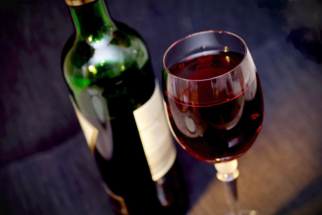 Glass of red wine beside a green wine bottle with a white label on a dark table