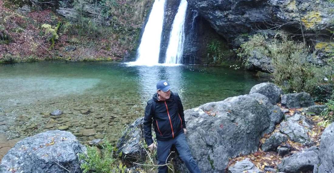 A hiker on the rocks by a waterfall and a clear green pool in the Enipeas gorge on Mount Olympus