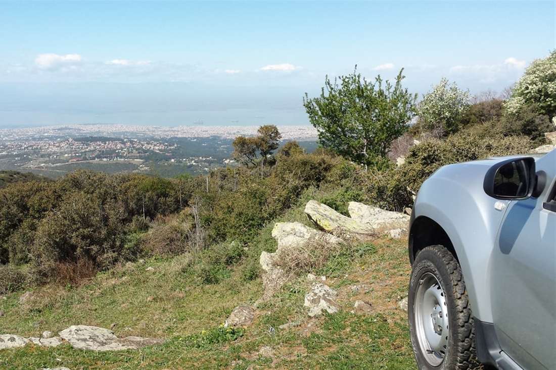 A silver SUV parked on a hillside track on Mount Chortiatis, with the city of Thessaloniki and the Thermaic Gulf below, on a Thessaloniki jeep safari.