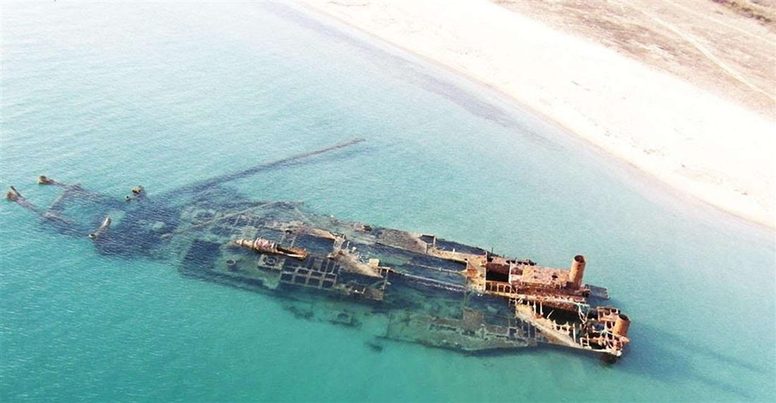 Aerial view of the rusted Epanomi shipwreck in shallow turquoise water beside a white sandy beach near Thessaloniki
