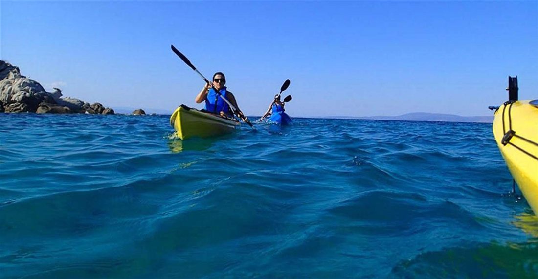 Two paddlers in yellow and blue sea kayaks on deep blue water of the Thermaic Gulf near Thessaloniki under a clear sky