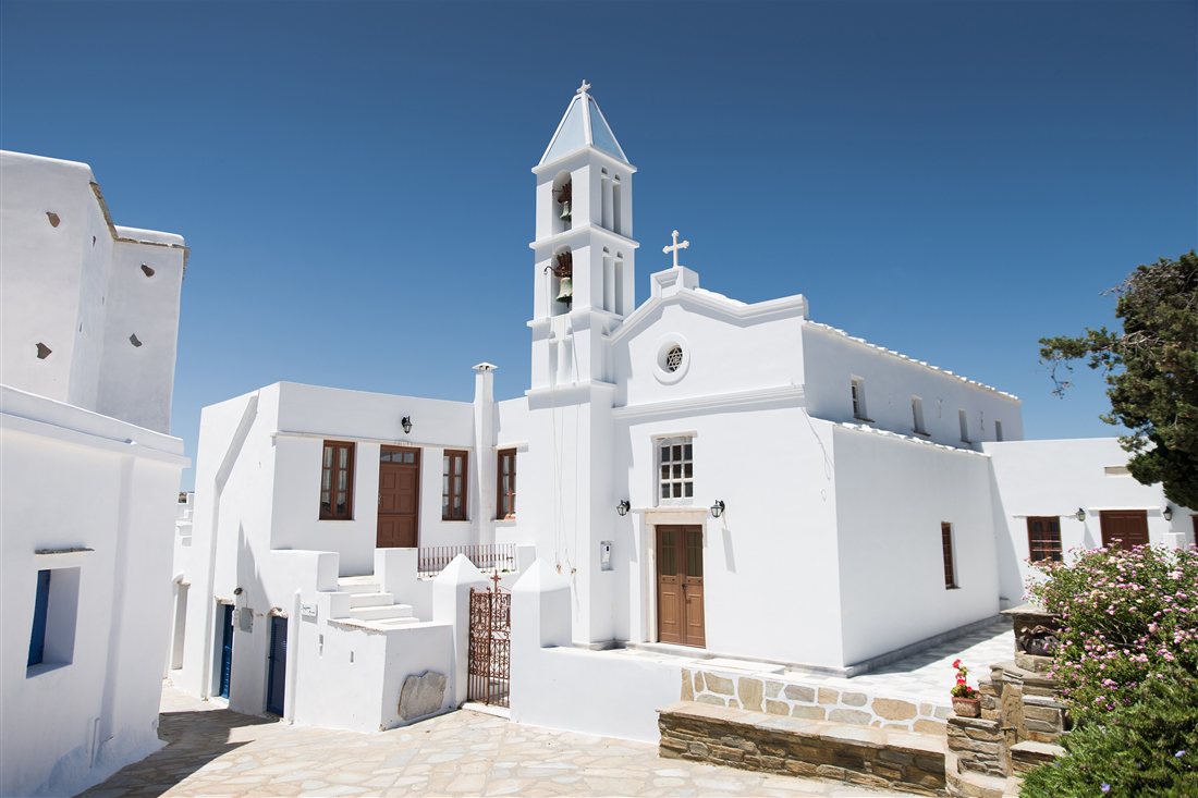 A white village church with a bell tower and a whitewashed courtyard on Tinos