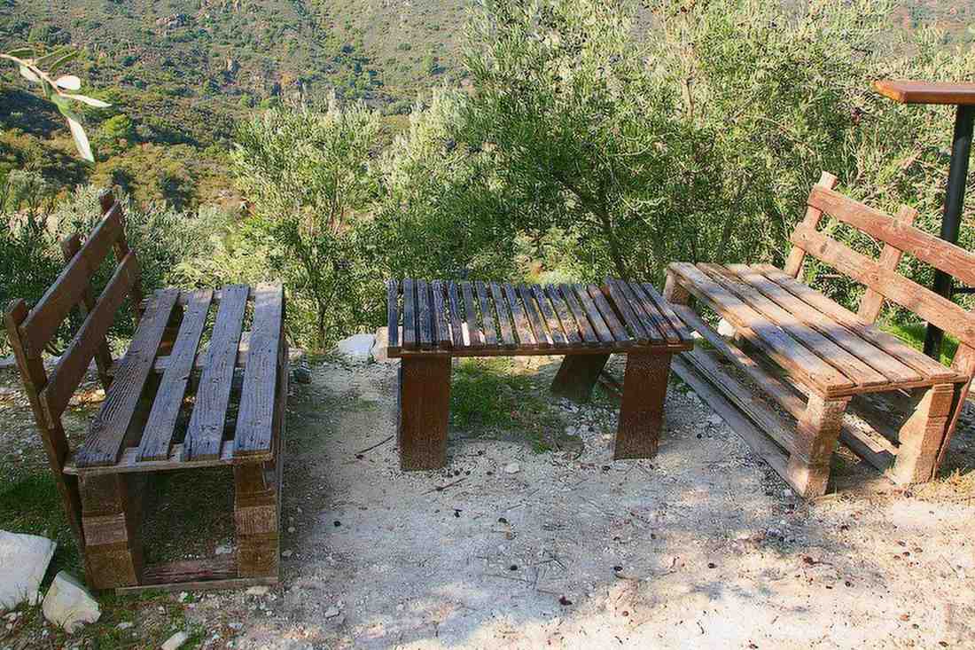 Wooden pallet benches and a low table on a terrace among olive trees above a green valley