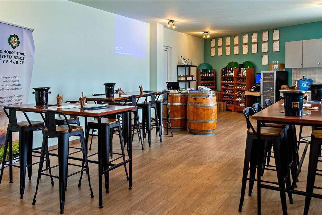 The tasting room of the Tyrnavos wine cooperative with high tables and wine shelves