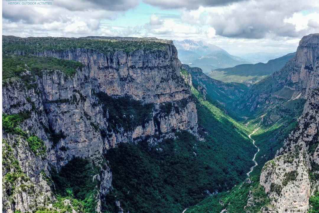 The deep Vikos Gorge in Zagori, with grey limestone cliffs and green forest running down to the river below.