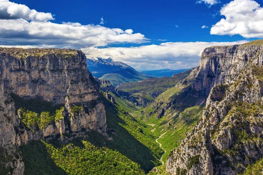 The Vikos Gorge cuts a deep green canyon between tall limestone walls under a blue sky in Zagori.