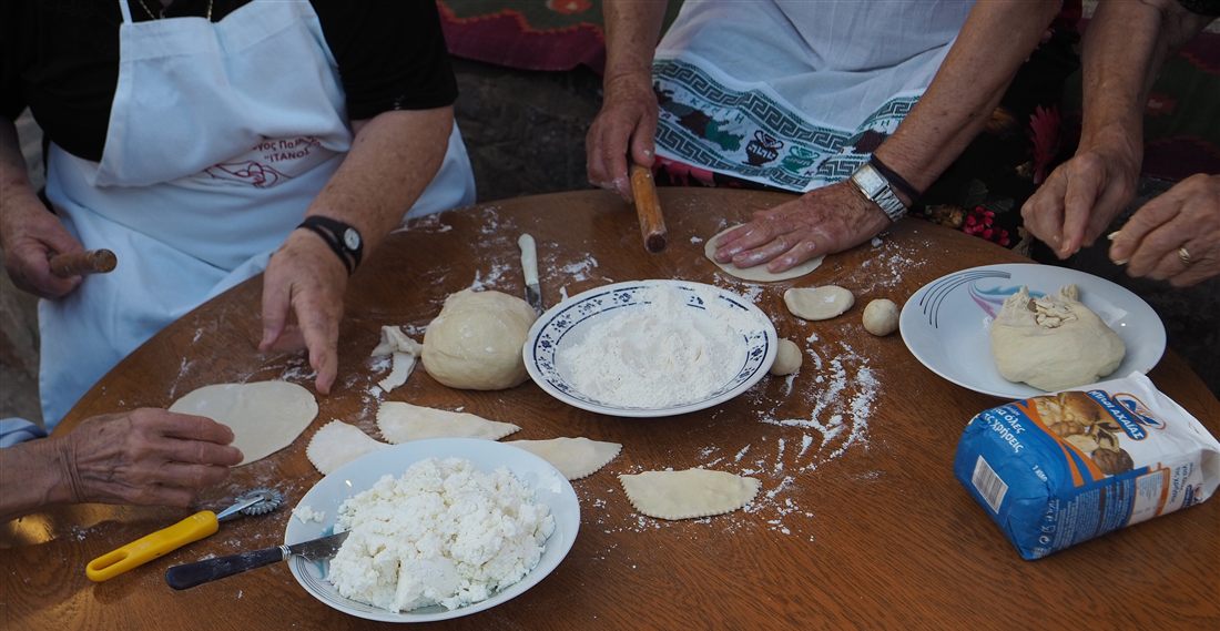 Hands rolling dough and folding cheese pies on a floured table in Greece, the same hands-on work guests do in a Zakynthos cooking class.