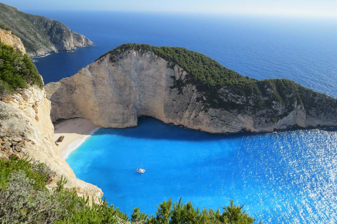 Navagio Shipwreck Beach on Zakynthos with white cliffs, turquoise water, the shipwreck on the sand and a boat anchored in the bay, seen from the clifftop viewing point