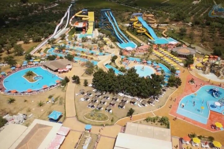 Aerial view of a Zakynthos water park with slide towers, pools, a lazy river and sunbeds among olive groves
