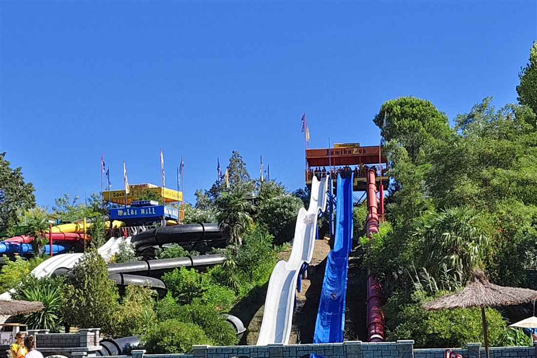 White, blue and red water slides running down a green hillside under a clear blue sky