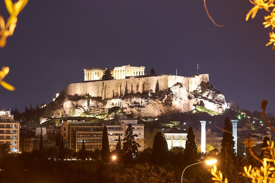 The illuminated Parthenon on top of the Acropolis hill at night, with Athens buildings below